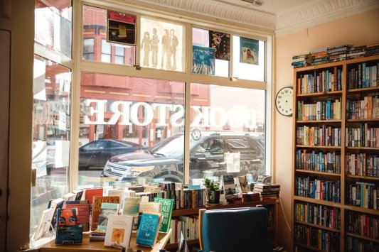 Fotografía de una librería desde dentro en la que se ve el escaparate principal, una mesa y varias estanterías